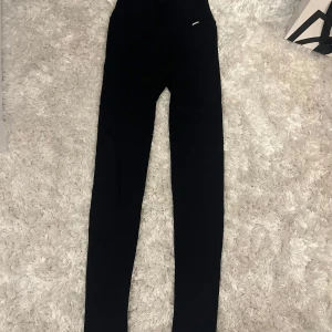Svarta Träningstights från Stronger - Svarta tights från Stronger i ribbat material. De är högmidjade och har en tight passform. Storlek xs. Tightsen är ändast använda ett fåtal gånger. Perfekta för träning eller chill dagar.