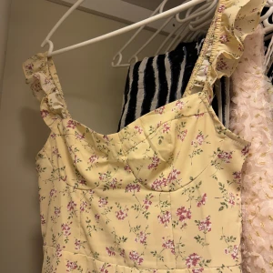 Ljusgul blommig klänning med volang - Säljer denna så söta ljusgula klänningen med blommor💕 står ej storlek men skulle säga S,  använd få gånger. Sitter fint på kroppen å har fina detaljer vid bysten och axelbanden. Även en slits vid ena benet. Perfekt lätt plagg på sommaren💓 Använd gärna KÖP NU