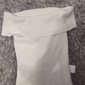 Vit ribbad offshoulder topp H&M - Säljer en vit ribbad offshoulder topp från H&M i storlek S. Toppen är axelbandslös med bred kant upptill och har en tight passform. 