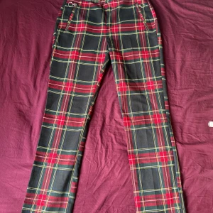 Röd- och svart-rutiga byxor - Snygga byxor med rött, svart och gult rutmönster. De har raka ben, dragkedjor vid fickorna och en klassisk midja. Perfekta för dig som vill sticka ut med en cool och färgstark stil.