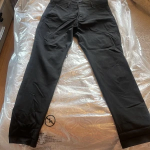 Svarta kostymbyxor i slim fit - Svarta kostymbyxor i slim fit med klassisk design och raka ben. Byxorna har hällor för bälte, fickor fram och bak samt stängs med dragkedja och knapp. Materialet är en mix av polyester, viskos och elastan för en skön stretchig känsla.