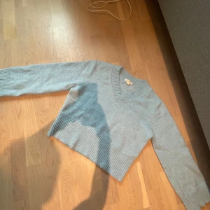 Ljusblå croppad stickad tröja - Superfin ljusblå stickad tröja med v-ringning och croppad passform. Tröjan har bred ribbad kant nedtill och vid ärmsluten, samt långa ärmar. 