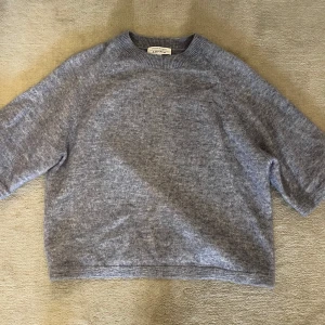 Blå stickad tröja från & Other Stories - Mysig blå stickad tröja från & Other Stories med rund halsringning och avslappnad passform. Tröjan har halvlånga ärmar och ribbade detaljer vid halsen. Perfekt för lager-på-lager under kyliga dagar.