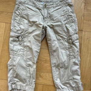 Beige cargoshorts från Esprit - Snygga beige cargoshorts från Esprit med flera fickor och dragkedjedetaljer. Modellen är midwaist och har avslappnad passform med resår vid benslut. Perfekta för sommarens äventyr och chill dagar utomhus.