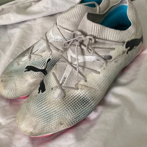 Puma Future Z 1.3 fotbollsskor vit/rosa - Säljer ett par Puma Future Z 1.3 fotbollsskor i storlek 43. Skorna är vita med svarta och blå detaljer, samt har en rosa sula med dobbar. Ovandelen är i syntetmaterial med snörning och stickad krage för skön passform. Perfekta för dig som vill sticka ut på planen.
