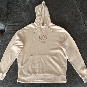 Beige hoodie från ASOS DESIGN XS - Snygg beige hoodie från ASOS DESIGN i storlek XS. Tröjan har huva med snörning, magficka och tryck med texten 'TAMPA Tennis Club Florida' framtill. Tillverkad i mjuk bomull, perfekt för chill dagar. Långärmad och loose fit för en avslappnad vibe.