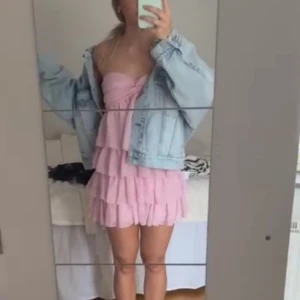 Rosa volangklänning axelbandslös - Supersöt rosa kortklänning med flera lager volanger och axelbandslös design. Klänningen har en twistad detalj vid bysten och är perfekt för dig som vill sticka ut. Lätt och luftig känsla, passar perfekt till varmare dagar.