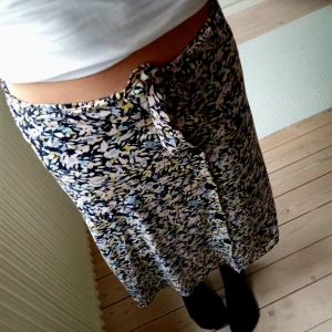 Omlottkjol - Sommrig omlottkjol från name it med blommigt mönster i blått, vitt, gult och svart. Kjolen har knyt i midjan🩷Storlek 152. Passar även xs🩷