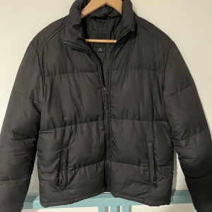 Svart pufferjacka från Brave Soul - Svart pufferjacka från Brave Soul London i storlek S. Jackan har hög krage, två fickor med dragkedja och quiltad design. Perfekt för kalla dagar med sin vadderade känsla och stilrena look. Stängs med dragkedja framtill. Öppen för bundles och frågor!  Man, kille, grisch, Stockholm, plagg, billigt, small, s, stil, stiligt, style, jacka, tröja, skjorta, kvalitet, märke, märkeskläder