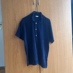 Mörkblå frottéskjorta från Brothers - Mörkblå skjorta från Brothers i mjuk frotté med korta ärmar och klassisk krage. Skjortan har knäppning framtill med vita knappar och en avslappnad passform.