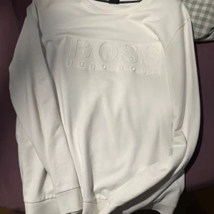 Vit sweatshirt från Hugo Boss - Säljer en stilren vit sweatshirt från Hugo Boss med upphöjt BOSS-tryck på bröstet. Väldigt bra skick användt knappast 