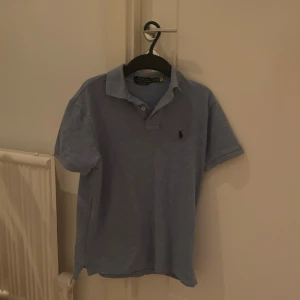 Blå pikétröja Polo Ralph Lauren XS - Snygg blå pikétröja från Polo Ralph Lauren i modellen Custom Slim Fit. Klassisk krage, korta ärmar och broderad logga på bröstet. Tillverkad i mjuk bomull som känns skön mot huden. Perfekt för en clean och stilren look.
