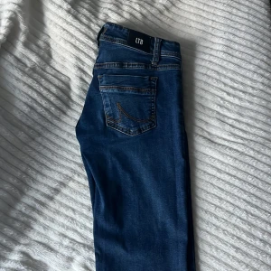 Mörkblå jeans från LTB - Snygga mörkblå jeans från LTB med klassisk femficksdesign och kontrastsömmar. Jeansen har en normal passform och är tillverkade i stretchigt denimtyg för extra komfort. Perfekta för dig som gillar en tidlös look med lite slitningar på benen. 