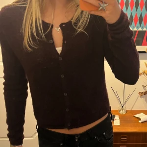 Vinröd  kofta från Gina Tricot - Säljer en mysig vinröd kofta från Gina Tricot i stickad ullmix. Koftan har långa ärmar, knappar hela vägen och en croppad passform som ger en trendig look. Perfekt att slänga över ett linne eller t-shirt för en chill vibe.