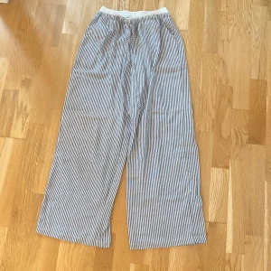 Randiga vida byxor från SHEIN - Längd 100cm.  Säljer ett par randiga, vida byxor från SHEIN i storlek S. Byxorna har resår i midjan och är i ett lätt och luftigt material, perfekta för varmare dagar. Svarta och vita smala ränder ger en klassisk look.