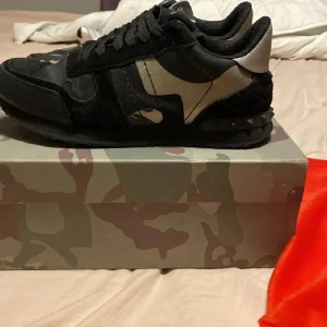 Valentino Rockrunners( intresse koll) - Snygga Valentino Rockrunner sneakers i svart och beige med kamouflagemönster och svarta detaljer. Skorna har rund tå, platt sula och klassisk snörning. Perfekta för dig som vill ha en unik och trendig look. Tar byten!