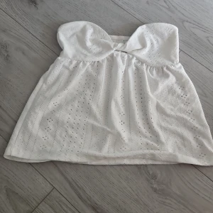 Vit tubtopp - Säljer en söt vit tubtopp med detaljer och lätt volang nedtill. Toppen är axelbandslös. Ingen aning vart den är ifrån, aldrig använd den då den inte passade mig💞