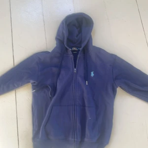Marinblå hoodie från Polo Ralph Lauren - Säljer en marinblå hoodie från Polo Ralph Lauren i modellen Custom Fit. Tröjan har dragkedja, huva med snörning och två fickor framtill. Klassisk broderad logga på bröstet i ljusblått. Perfekt nu inför för sommaren☀️