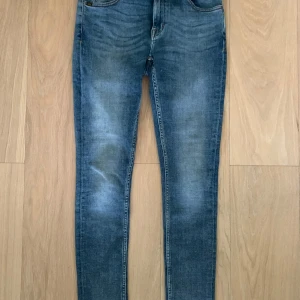 Blå skinny jeans - Säljer ett par klassiska blå skinny jeans med lätt slitning och normalhög midja. Jeansen har fem fickor och stängs med dragkedja och knapp. Perfekta till vardags och enkla att matcha med olika toppar.