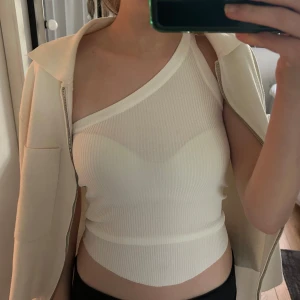 Vit ribbad oneshoulder topp från Zara - Säljer en vit ribbad oneshoulder topp från Zara. Snygg och trendig modell med asymmetrisk axel och tight passform. Perfekt att styla till både jeans och kjol. Fräsch och stilren look!