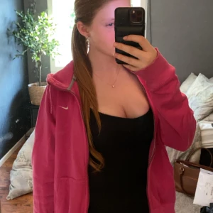 Rosa zip-hoodie från Nike - Säljer en rosa hoodie med dragkedja från Nike. Jackan har lång ärm, ribbade muddar och en klassisk hoodie-passform. Perfekt för en avslappnad stil och enkel att matcha med jeans eller leggings.