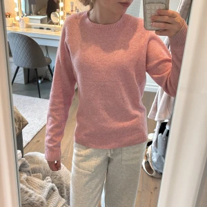 Rosa stickad tröja från Vero Moda. Använd två gånger - Mysig rosa stickad tröja från Vero Moda med rund halsringning och långa ärmar. Tröjan har en enkel och klassisk design med ribbade muddar vid ärmslut och nederkant. Perfekt för lager-på-lager och passar till många olika stilar.