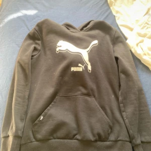 Svart Puma set  - Svart hoodie från Puma med stor vit logga framtill. Klassisk känguruficka och huva. Mjuk insida och ribbade muddar vid ärmslut och nederkant. Perfekt för en sportig och avslappnad stil.