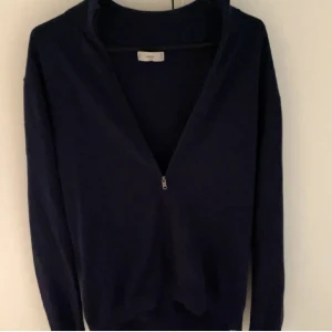 Mörkblå stickad tröja med dragkedja från MGN - Säljer en mörkblå långärmad tröja från MGN med halv dragkedja framtill. Tröjan har en klassisk passform och är perfekt för vardagen. Enkel och stilren design som passar till mycket.