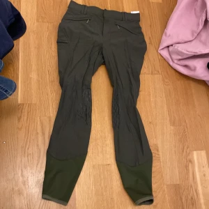 Mörkgröna ridbyxor från Hööks - Säljer ett par mörkgröna ridbyxor från Hööks med förstärkta partier på insidan av benen och knäna. Byxorna har hög midja, dragkedjefickor fram och diskret H-logga bak. Perfekta för ridning och har snygga detaljer med silikonmönster för extra grepp.