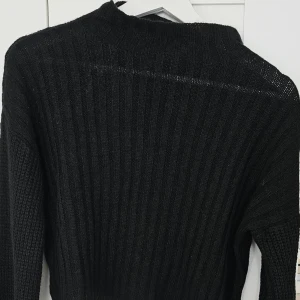 Svart croppad stickad tröja - Säljer en svart croppad stickad tröja med lång ärm och ribbad struktur. Perfekt för lager-på-lager och passar till både jeans och kjol. Enkel och stilren design som funkar till många outfits.