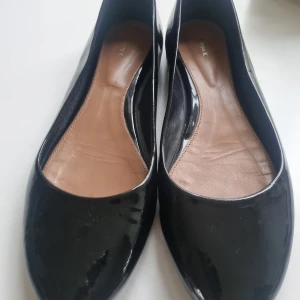 Svarta ballerinaskor från Filippa K - Säljer ett par klassiska svarta blanka ballerinaskor från Filippa K i skinn. Skorna har rund tå och en stilren design med glansig finish. Perfekta för dig som gillar enkel och tidlös stil. Små i storleken, snarare 39,5 än 40. Nypris 2000 kr. Använda ett fåtal gånger.