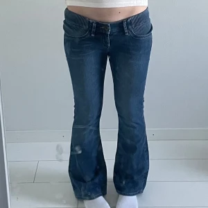 Blå bootcut jeans med randiga detaljer - Säljer ett par blå bootcut jeans med unika randiga detaljer vid fickorna och midjan. Jeansen har klassisk femficksdesign, knapp- och dragkedjestängning samt normal passform. Perfekta för dig som vill ha en cool och avslappnad stil.