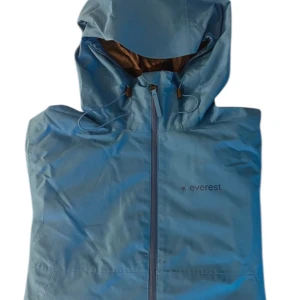Blå vindjacka från Everest - Snygg blå vindjacka från Everest med huva och dragkedja framtill. Perfekt för blåsiga dagar och outdoor-aktiviteter. Jackan har minimalistisk design och justerbar huva för extra skydd.