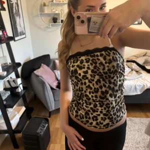 Leopardmönstrad tubtopp med spetskant - Säljer en snygg leopardmönstrad tubtopp med svart spetskant upptill och en liten rosett. Toppen är figurnära och perfekt för att sticka ut. Materialet känns mjukt och stretchigt.
