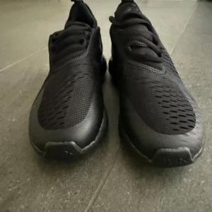 Svarta Nike Air Max 270 sneakers - Säljer ett par oanvända helsvarta Nike Air Max 270 sneakers med mesh-överdel och synlig Air-enhet i hälen. Skorna har snörning och en sportig, modern design som passar perfekt till streetwear och träning.