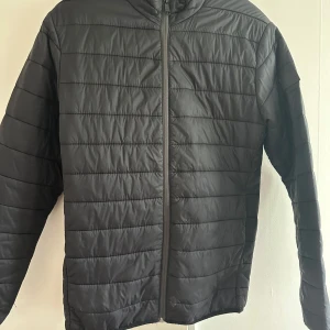Svart pufferjacka från Jack & Jones i mkt bra skick - Säljer en svart pufferjacka från Jack & Jones i storlek S. Jackan har lång ärm, dragkedja framtill och ett stilrent, quiltat mönster. Perfekt för kyligare dagar och enkel att matcha med olika outfits.
