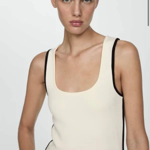 Vit ribbad linnetopp från Mango - Säljer en vit ribbad linnetopp från Mango med svarta kontrastkanter. Toppen har en rundad halsringning och är ärmlös, perfekt för varma dagar eller som lager på lager-plagg. NYPRIS 380kr!! Storlek M🥰