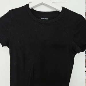 Svart ribbad t-shirt från Even&Odd - En svart ribbad t-shirt från Even&Odd med rund halsringning och korta ärmar. Enkel och stilren modell som passar till mycket. Perfekt basplagg i garderoben.