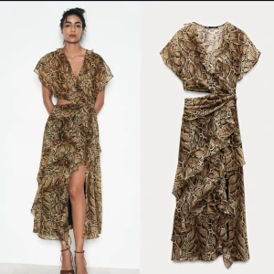 Brun omlottklänning med ormmönster - Säljer en snygg omlottklänning med brunt ormmönster och volangdetaljer. Klänningen har korta ärmar, v-ringning och en hög slits framtill. Perfekt för dig som vill sticka ut med ett djurmönster och en feminin siluett.