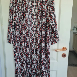 Mönstrad lång kimono från Vila - Säljer en lång kimono från Vila med svart, vit och röd grafiskt mönster. Kimono har lång ärm och en lös passform, perfekt för dig som gillar statement-plagg med mycket mönster.