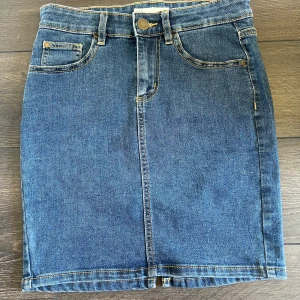 Jeanskjol från Cubus - Snygg klassisk blå jeanskjol från Cubus med fem fickor och knappstängning framtill. Kjolen har bälteshällor och en liten slits bak för extra rörelsefrihet. Perfekt till vardags med en t-shirt eller stickad tröja.