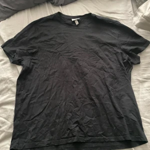 Svart slim fit t-shirt från H&M - En klassisk svart t-shirt från H&M i slim fit-modell. T-shirten har rund halsringning och korta ärmar, perfekt för en enkel och stilren look. Passar till det mesta och är ett måste i garderoben.