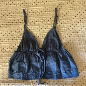 Blå croppad linnetopp - Säljer en blå croppad linnetopp med smala justerbara axelband och knytning framtill. Toppen har dekorativa sömmar. Toppen har knappt använts och är i mycket bra skick.