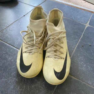 Beige Gul Nike Mercurial fotbollsskor - Säljer ett par beige Nike Mercurial fotbollsskor med högt skaft och stora svarta Nike-loggor på sidorna. Skorna har snörning och är designade för att ge bra grepp på planen. Perfekta för dig som vill sticka ut på fotbollen! Andvända några enstaka gånger.👍🏻Går att diskutera pris👍🏻