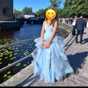 Ljusblå volangklänning med v-ringning - Säljer en drömmig ljusblå långklänning med flera lager volanger och v-ringad överdel. Klänningen har en markerad midja och är ärmlös, perfekt för bal. Materialet är lätt och ger ett svävande intryck. Använd 2 gånger. Skulle säg att den sitter som en S/XS. Finns dragkedja där bak. Jag är ca 167 cm lång. Och hade på mig ballerina skor. Köptes för 2200 men säljer för 1100
