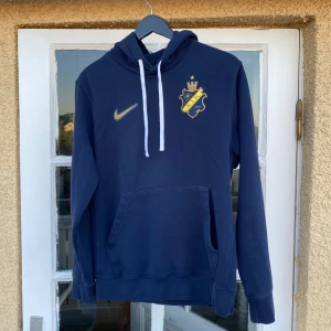 2022 Nike AIK Stockholm Hoodie (S) - Hoodies är äkta, köpt från aiks shop, från sesong 2022. Tröjan är i mycket bra skick utan några fläckar. Tvättlappen på insidan är bortklippt. Material 20% polyester 80% bomull. Tveka inte på att ställa några frågor.