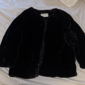 Svart fuskpälsjacka från VILA - Säljer en svart fuskpälsjacka från VILA. Jackan har en klassisk rak passform och är helsvart med mjuk pälsimitation. Perfekt för att ge en lyxig känsla till din outfit. Stängs framtill och har lång ärm.