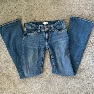 Blå bootcut jeans från Gina Tricot - Säljer ett par klassiska blå jeans från Gina Tricot i modell bootcut. Jeansen har fem fickor, snygga kontrastsömmar och dekorativa ficklock bak med knappdetalj. Defekter på de två sista bilderna. Men syns knappt! Användt ungefär 2 gånger i skolan. Skriv privat om du har frågor! Midjemåttet är 35 rakt över💕