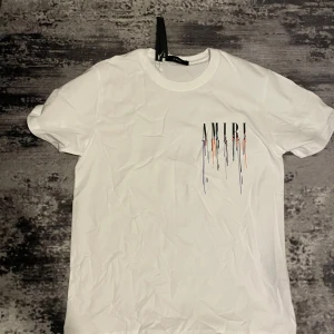 2 amiri t shirt - Säljer en vit t-shirt från Amiri med ett färgglatt, droppande logotyptryck på bröstet. T-shirten har rund halsringning och korta ärmar. Perfekt för dig som gillar streetwear och vill sticka ut med en snygg detalj.