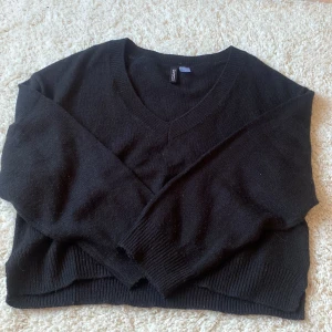 Svart stickad tröja från H&M Divided - Svart stickad tröja från H&M Divided med v-ringad hals och långa ärmar. Tröjan har en enkel och klassisk design med ribbade muddar vid ärmslut och nederkant. Perfekt för lager-på-lager och passar till det mesta.